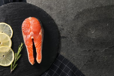 Photo of Fresh salmon steak, rosemary and lemon on dark textured table, top view. Space for text