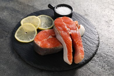 Photo of Fresh salmon steaks, salt and lemon on dark textured table, closeup