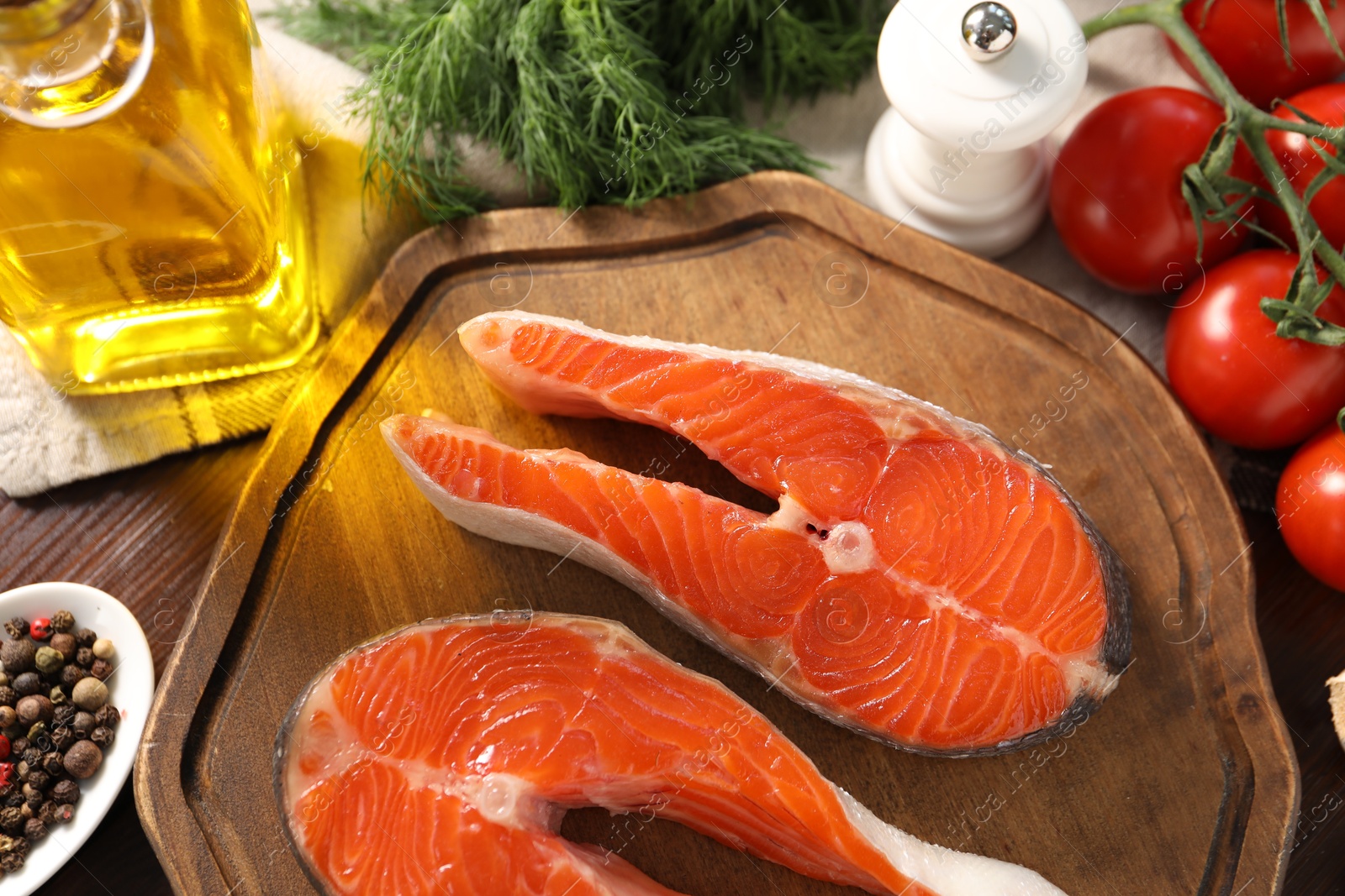 Photo of Board with fresh salmon steaks, peppercorns and products on wooden table, flat lay