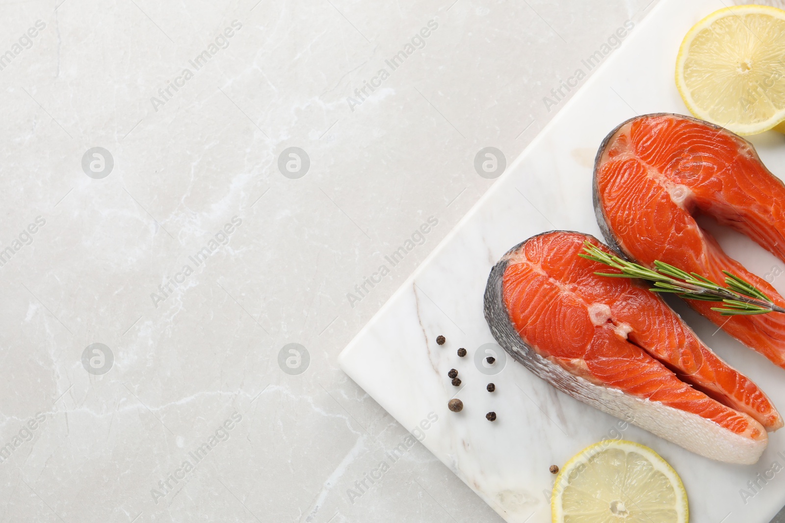 Photo of Board with fresh salmon steaks, peppercorns, rosemary and lemon on light marble table, top view. Space for text