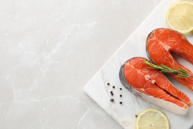 Photo of Board with fresh salmon steaks, peppercorns, rosemary and lemon on light marble table, top view. Space for text