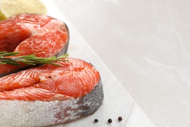 Photo of Board with fresh salmon steaks, peppercorns and rosemary on light marble table, closeup. Space for text