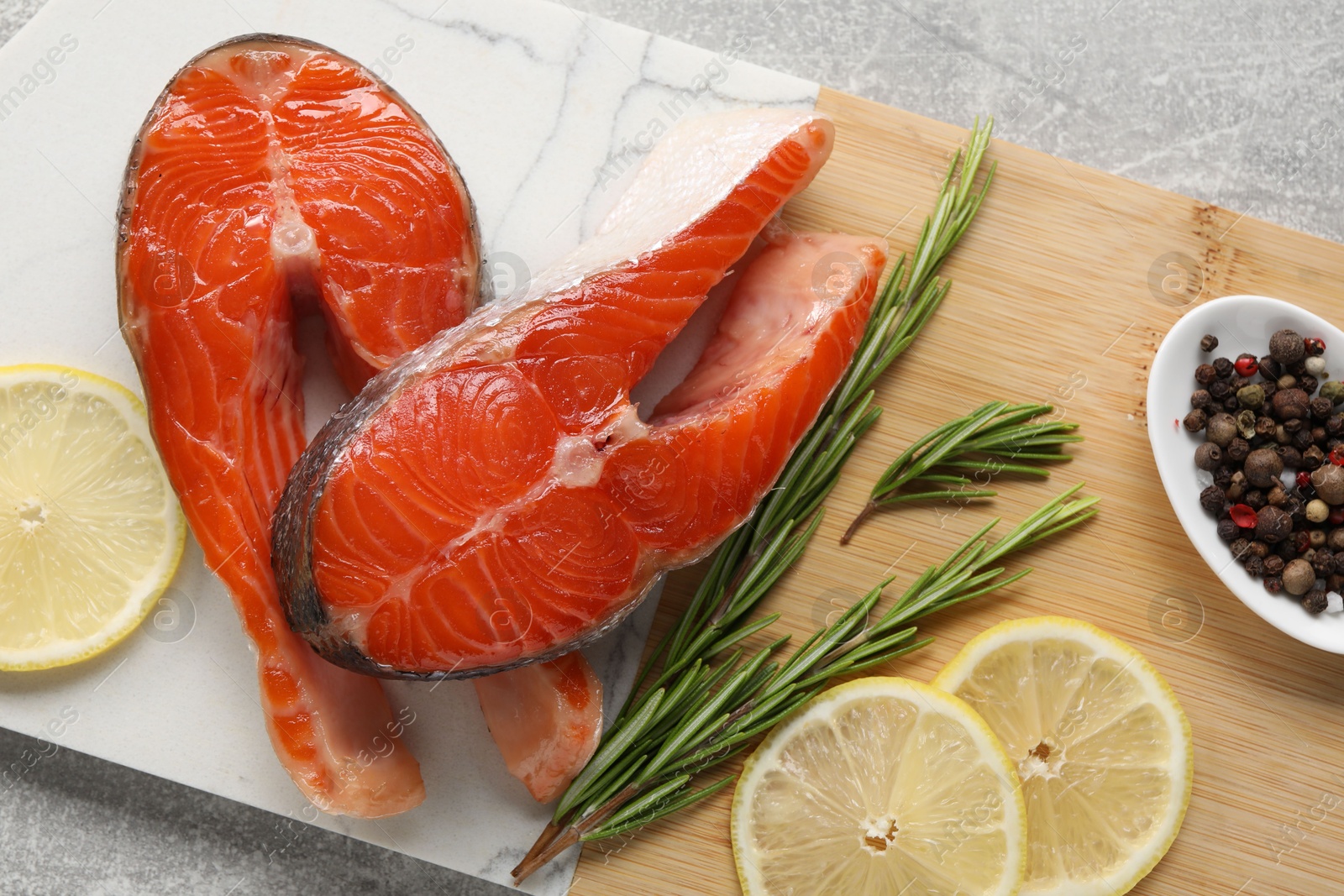 Photo of Board with fresh salmon steaks, peppercorns, rosemary and lemon on grey textured table, top view