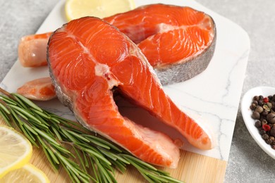 Board with fresh salmon steaks, peppercorns, rosemary and lemon on grey table, closeup