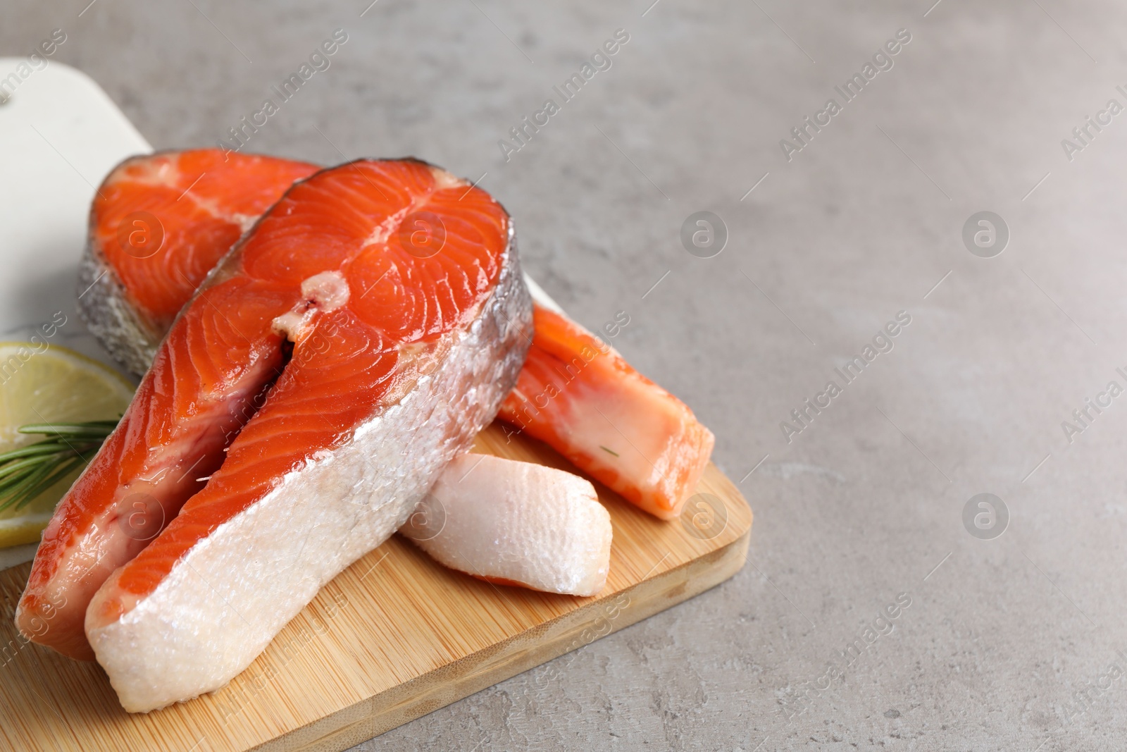 Photo of Board with fresh salmon steaks, rosemary and lemon on grey textured table, closeup. Space for text