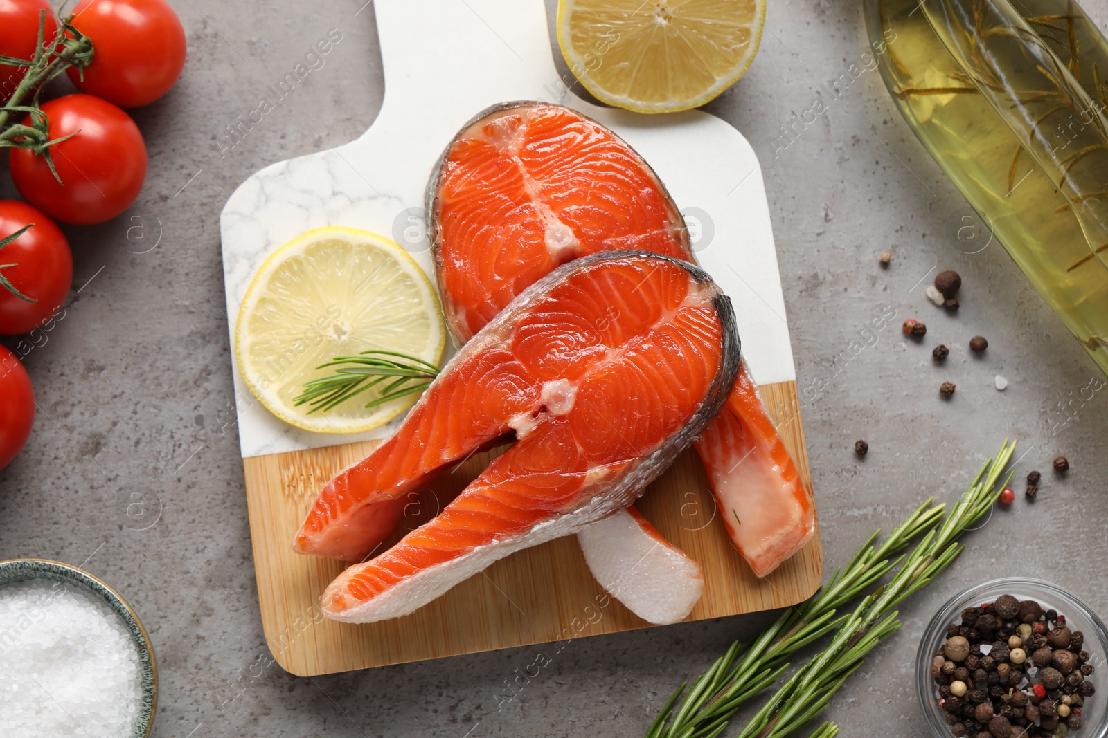 Photo of Board with fresh salmon steaks, rosemary and lemon on grey textured table, flat lay