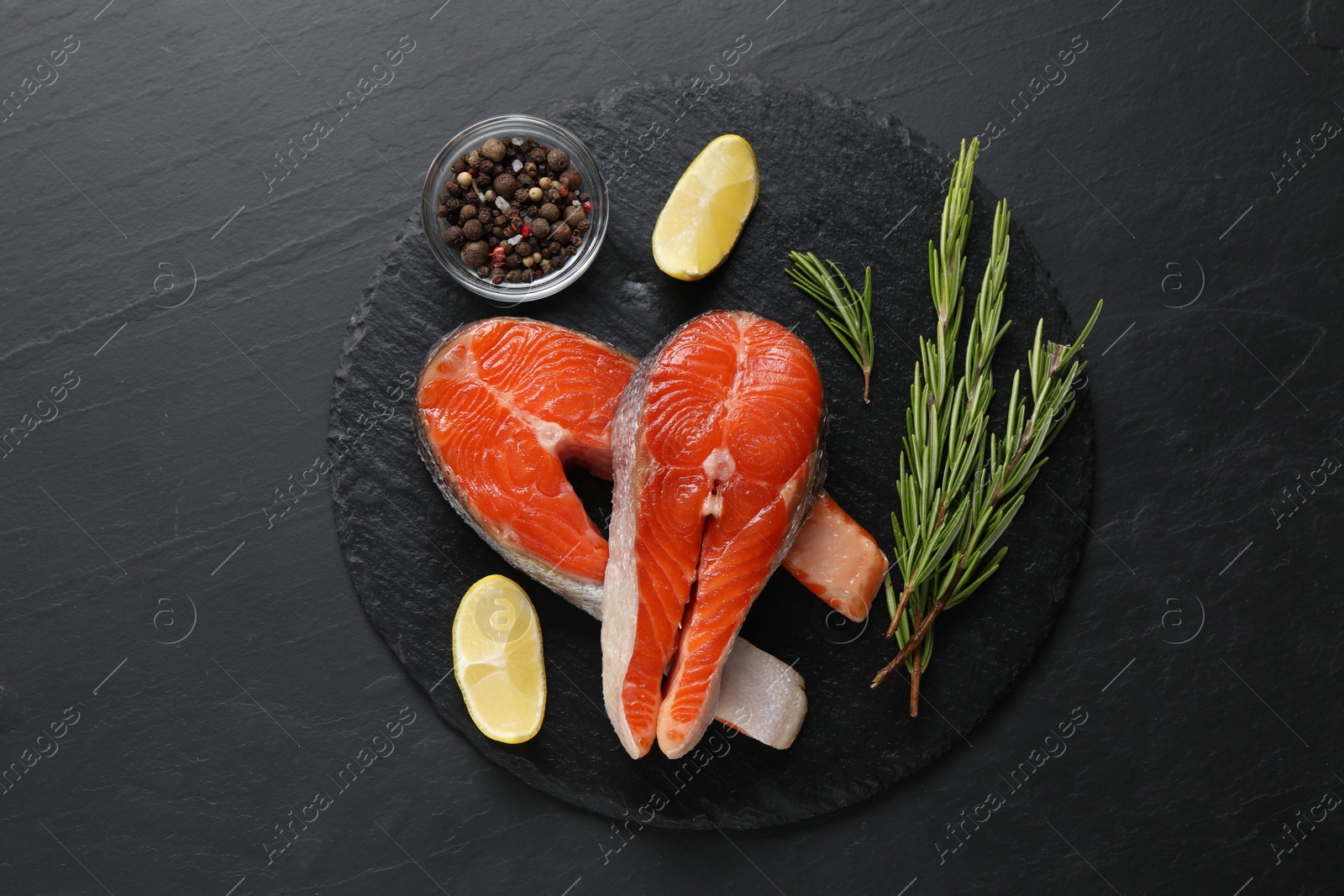 Photo of Fresh salmon steaks, rosemary, peppercorns and lemon on dark textured table, flat lay