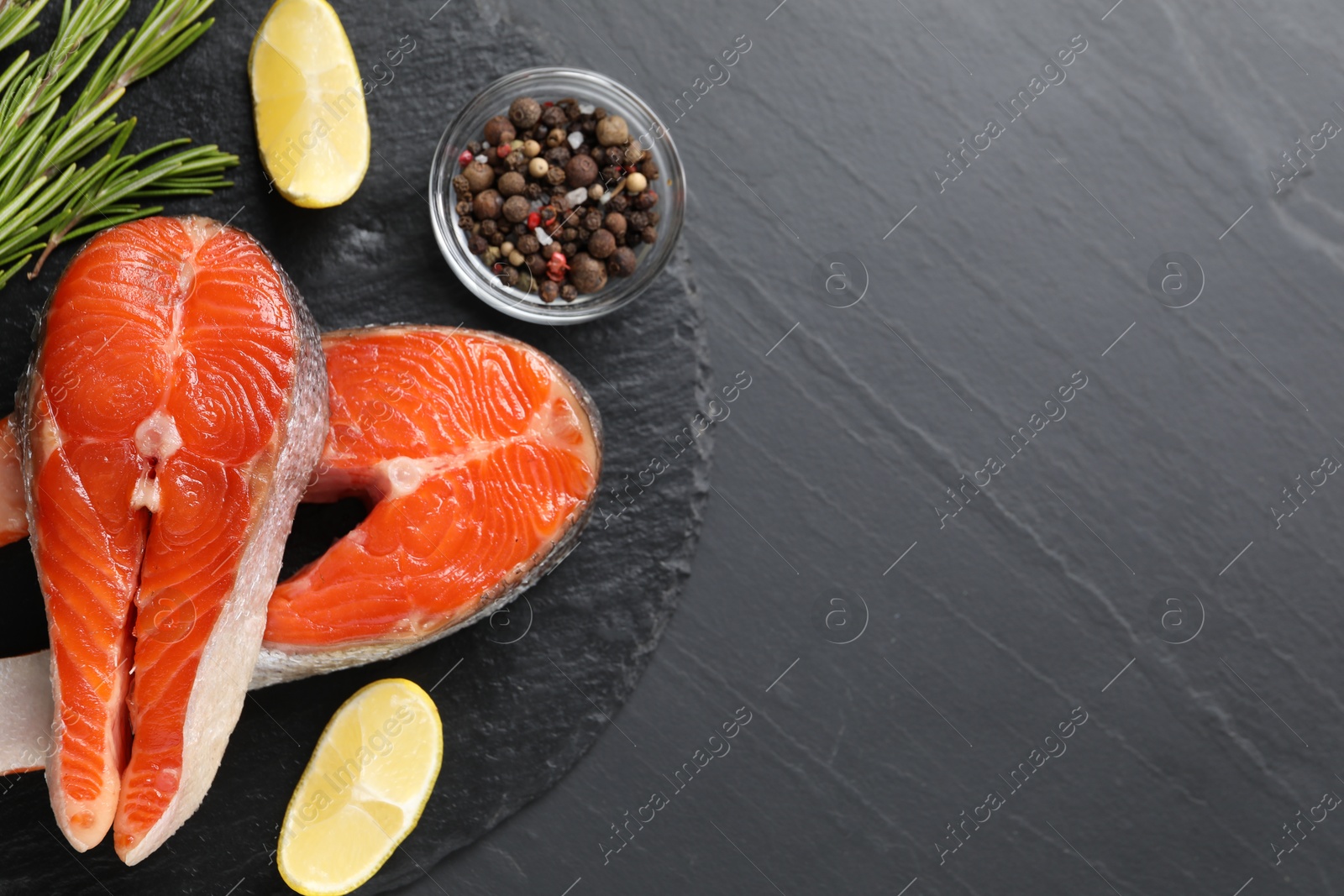 Photo of Fresh salmon steaks, rosemary, peppercorns and lemon on dark textured table, flat lay. Space for text