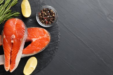 Photo of Fresh salmon steaks, rosemary, peppercorns and lemon on dark textured table, flat lay. Space for text