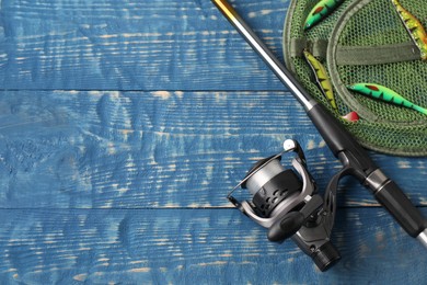 Fishing spinning, net and lures on blue wooden background, flat lay. Space for text