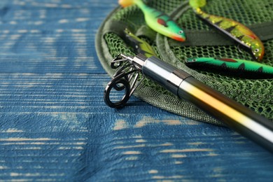 Photo of Fishing spinning, net and lures on blue wooden table. Space for text