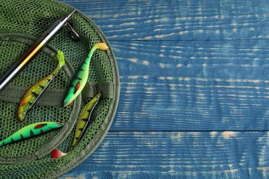 Fishing spinning, net and lures on blue wooden background, flat lay. Space for text