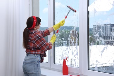 Photo of Woman with squeegee tool and foam cleaning window indoors