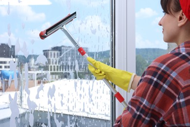 Woman with squeegee tool and foam cleaning window indoors