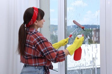 Woman with squeegee tool and foam cleaning window indoors