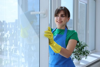 Beautiful young woman with napkin cleaning window indoors