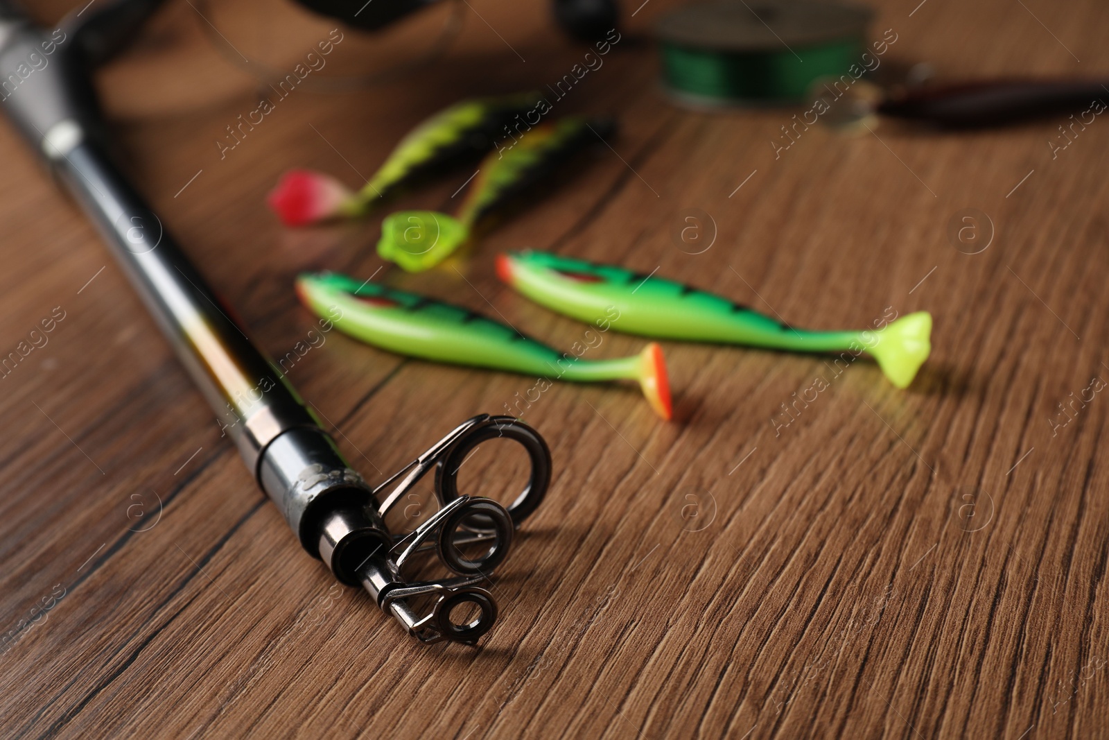 Photo of Fishing rod and baits on wooden table, closeup