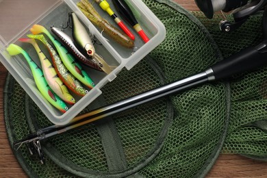 Photo of Fishing rod with spinning reel, baits, floats and net on wooden table, top view