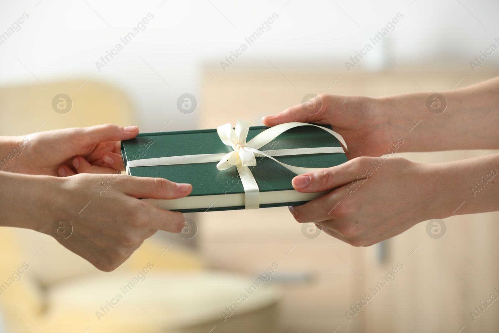 Photo of Woman gifting her friend book tied with beige ribbon indoors, closeup