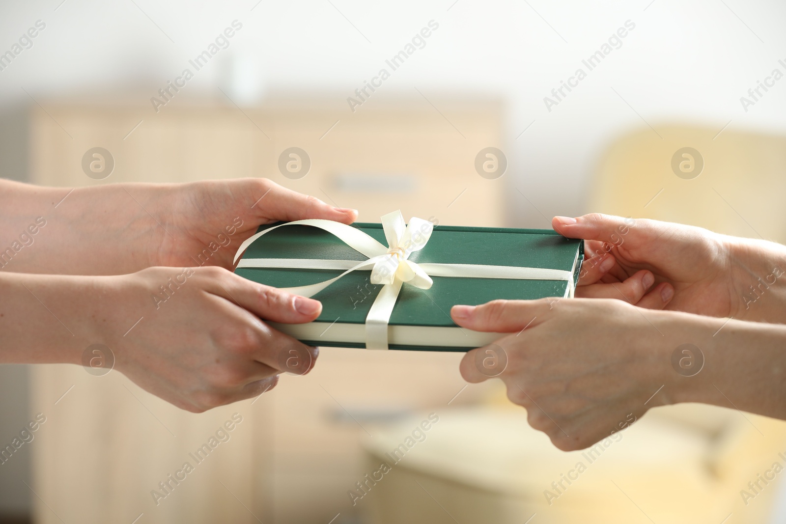 Photo of Woman gifting her friend book tied with beige ribbon indoors, closeup