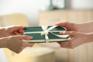 Photo of Woman gifting her friend book tied with beige ribbon indoors, closeup