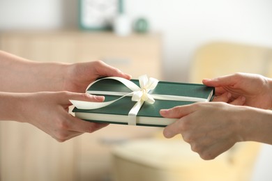 Woman gifting her friend book tied with beige ribbon indoors, closeup