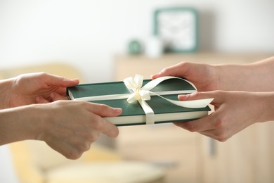 Photo of Woman gifting her friend book tied with beige ribbon indoors, closeup