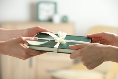 Photo of Woman gifting her friend book tied with beige ribbon indoors, closeup