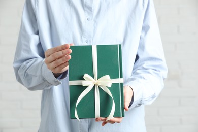 Photo of Woman holding book tied with beige ribbon as gift indoors, closeup