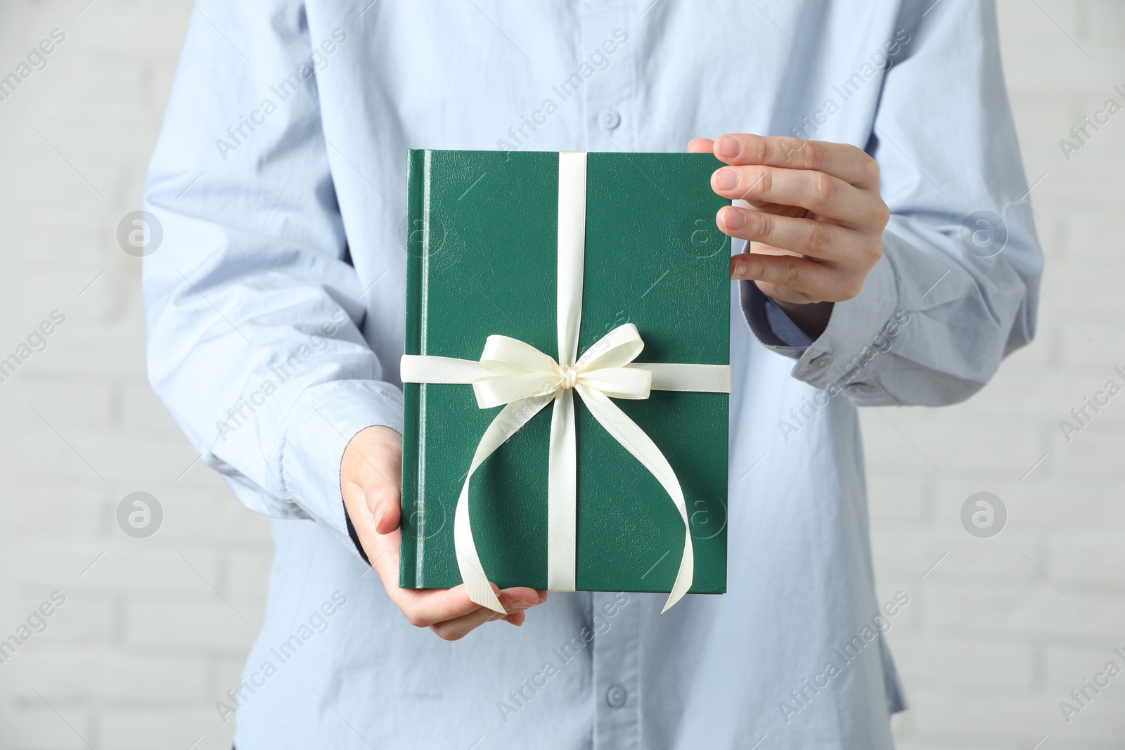 Photo of Woman holding book tied with beige ribbon as gift indoors, closeup