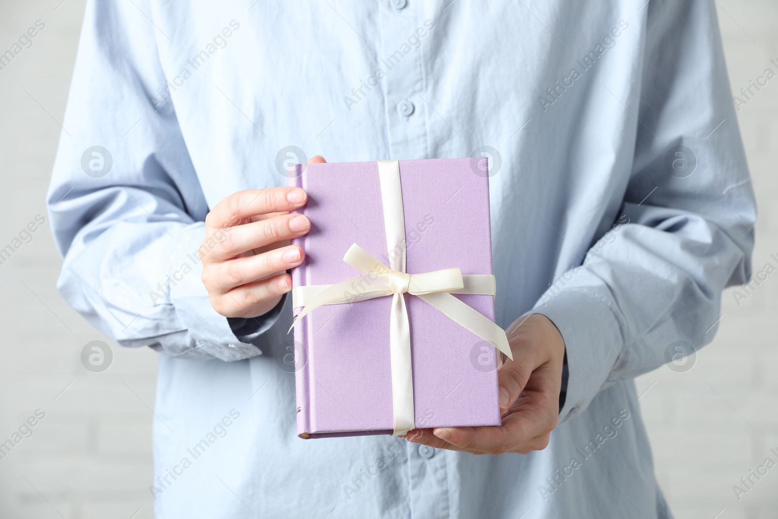 Photo of Woman holding book tied with beige ribbon as gift indoors, closeup