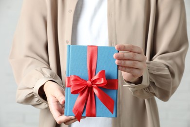 Woman holding book tied with red ribbon indoors, closeup