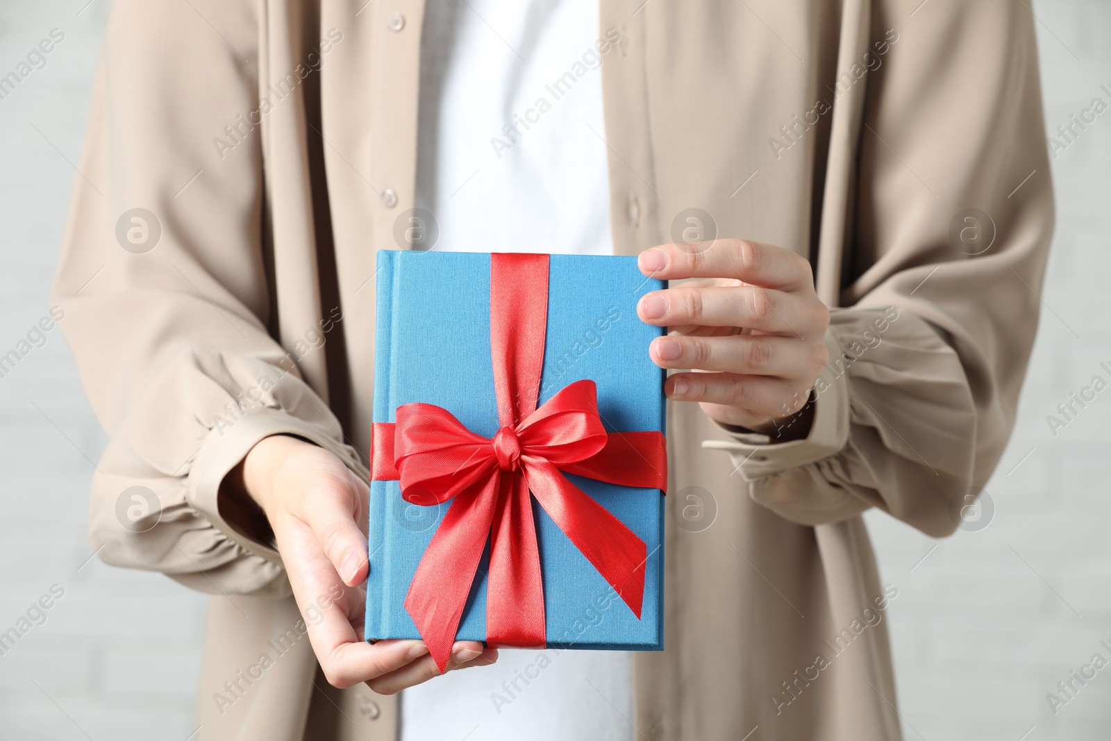 Photo of Woman holding book tied with red ribbon indoors, closeup