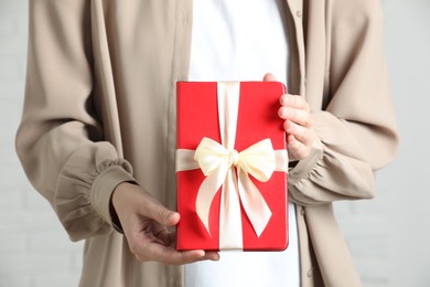 Photo of Woman holding book tied with beige ribbon as gift indoors, closeup