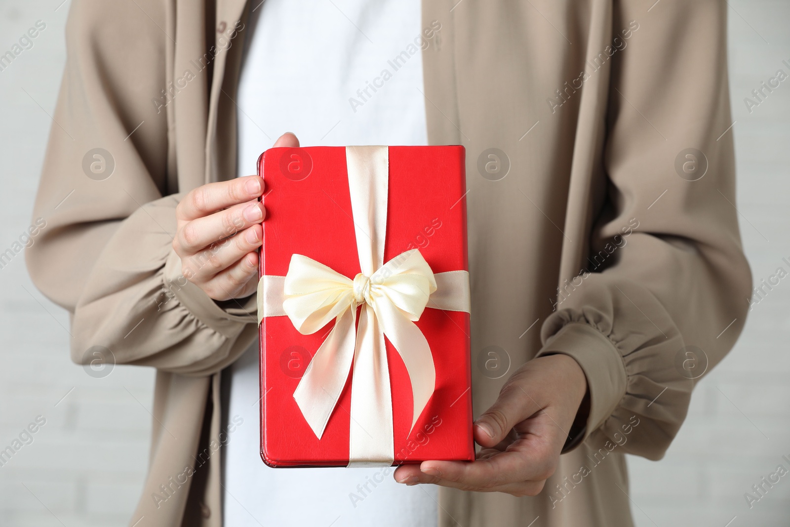 Photo of Woman holding book tied with beige ribbon as gift indoors, closeup