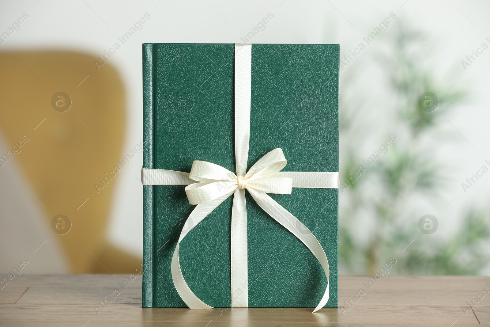 Photo of Book tied with beige ribbon as gift on wooden table indoors