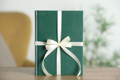 Photo of Book tied with beige ribbon as gift on wooden table indoors