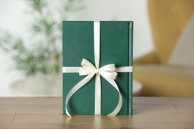 Photo of Book tied with beige ribbon as gift on wooden table indoors