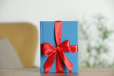 Photo of Book tied with red ribbon as gift on wooden table indoors