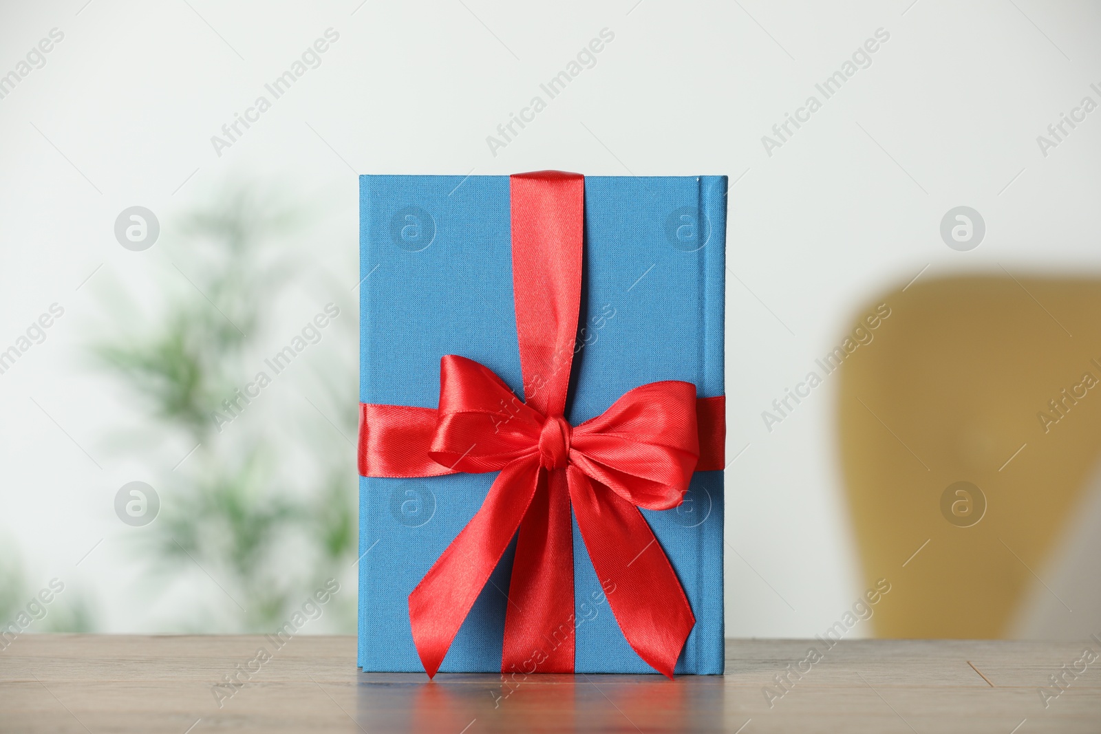 Photo of Book tied with red ribbon as gift on wooden table indoors