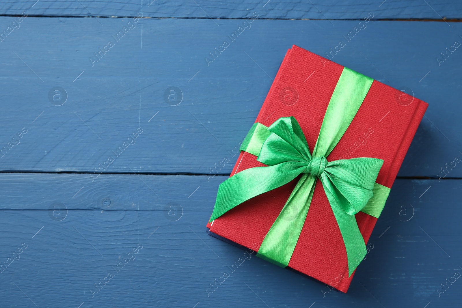 Photo of Books tied with green ribbon as gift on blue wooden table, top view. Space for text