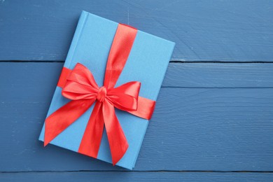 Photo of Book tied with red ribbon as gift on blue wooden table, top view. Space for text