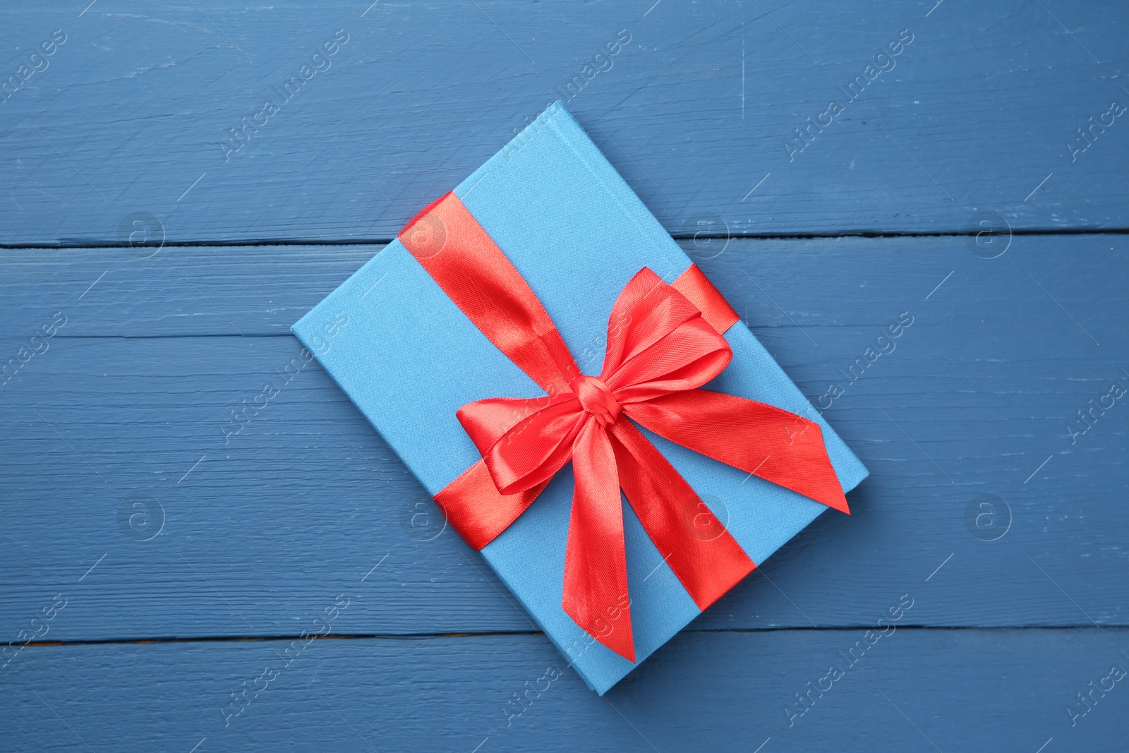 Photo of Book tied with red ribbon as gift on blue wooden table, top view