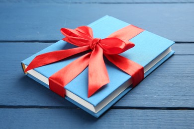 Photo of Book tied with red ribbon as gift on blue wooden table