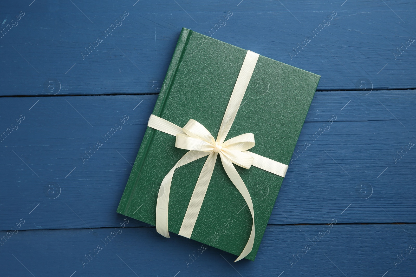 Photo of Book tied with beige ribbon as gift on blue wooden table, top view