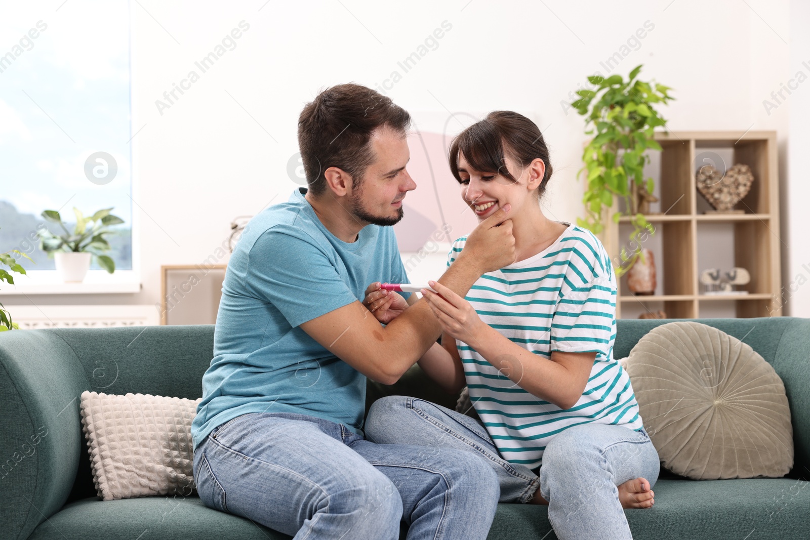 Photo of Happy young couple with pregnancy test on sofa at home