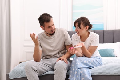 Photo of Worried young couple with pregnancy test on bed at home