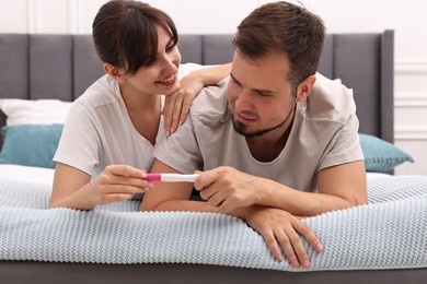 Happy young couple with pregnancy test on bed at home