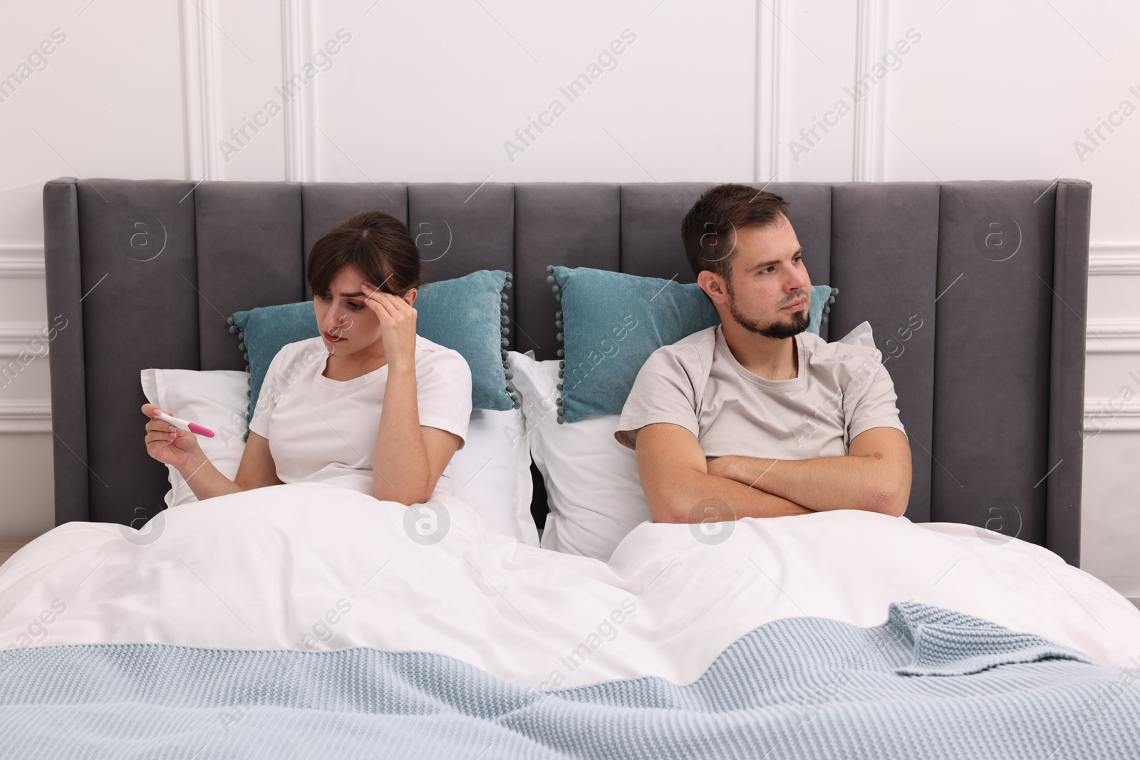 Photo of Worried young couple with pregnancy test on bed at home