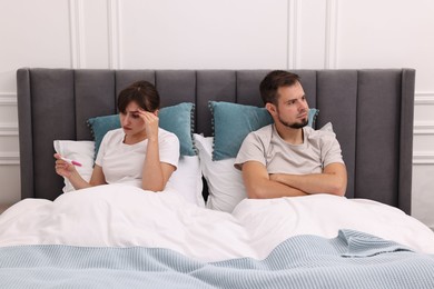 Worried young couple with pregnancy test on bed at home